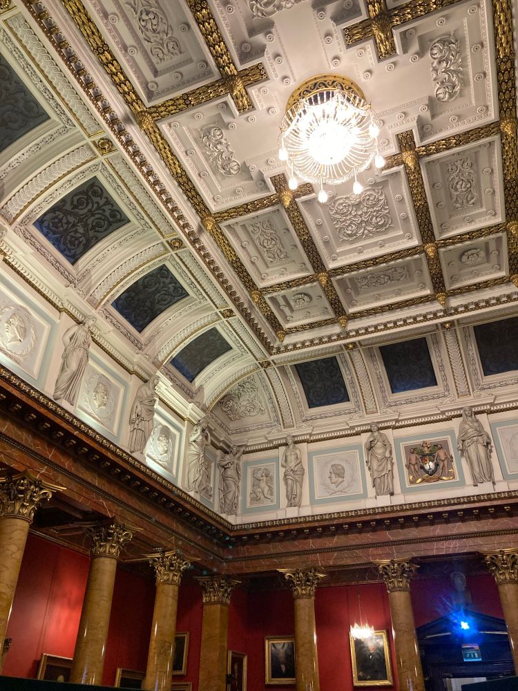 The ornate ceiling of the Great Hall featuring gold pillars, statues, elaborate plasterwork and a chandelier.