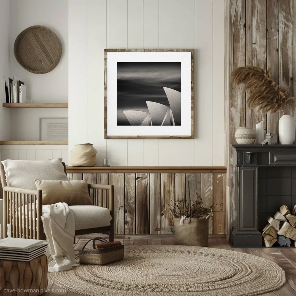 A monochrome photograph of the Sydney Opera House roof hangs as a framed print in a rustic living room, its semi-abstract design complementing the space's natural textures. The intricate geometric patterns and flowing lines of the iconic architecture contrast elegantly with the room's earthy tones and weathered wood. Light and shadow interplay within the image, creating a striking focal point that balances modern artistry with the cozy warmth of the setting.