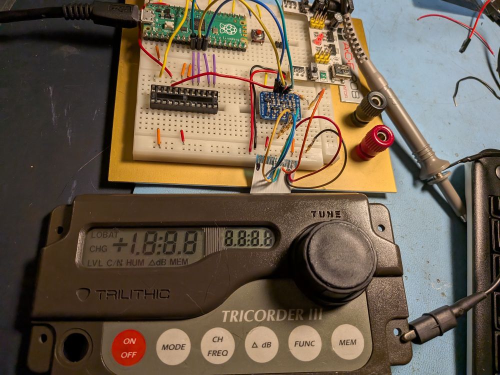 A brown front panel hooked up to a Raspberry Pi Pico through a level shifter.  The display has 7.5 digits, decimals and other lit up segments. Also on the panel are six buttons and a large round dial.