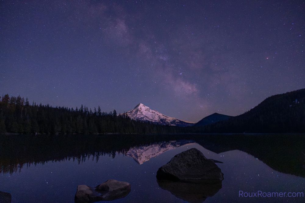 Milky way arching over Mt Hood with a silhouette forest surrounding a lake foreground
