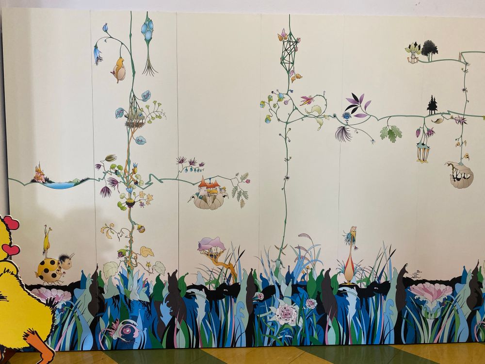 Quelques panneaux du papier peint créé par Claude Ponti. Au sol des herbes et des fleurs, parfois quelques tiges s’élancent vers le haut puis à gauche ou à droite, portant des feuilles, fleurs, ou étranges maisons.