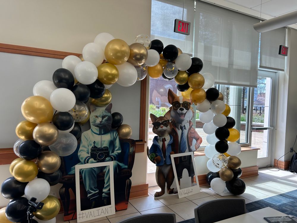 A balloon arch with AI-generated cut outs of a cat Val and a dog Ian. 
