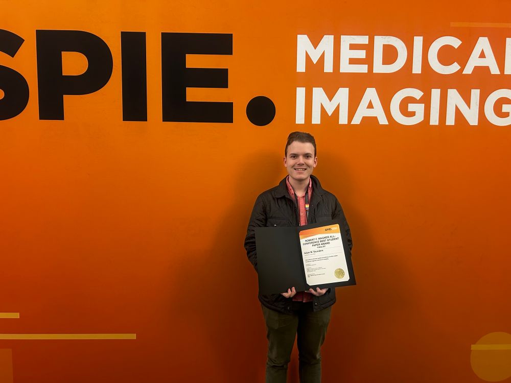 I am standing with a certificate next to a large sign saying “SPIE Medical Imaging”