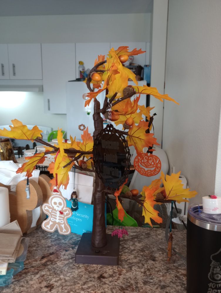 A fake tree with autumn leaves and Halloween-themed small ornaments on the branches.