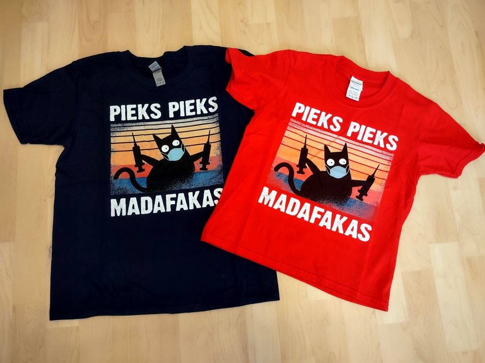 Ein schwarzes und ein rotes T-Shirt liegen auf dem Boden. Auf den T-Shirts ist jeweils eine schwarze Katze mit Maske und zwei Spritzen in den Pfoten abgebildet. Auf den T-Shirts steht: Pieks Pieks Madafakas