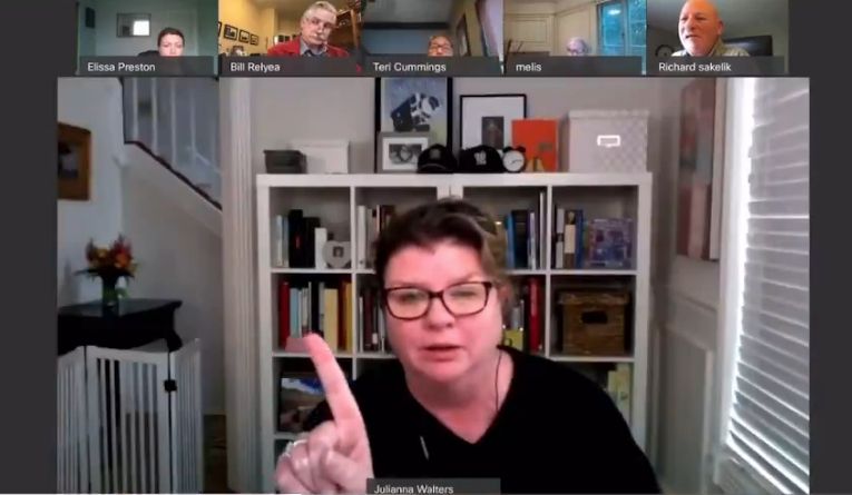 A middle aged white woman on a zoomcall from her home. She is wagging her finger at the screen.