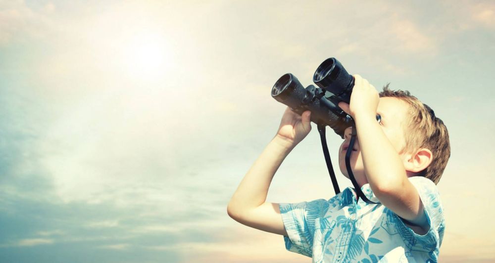 a boy looks into the sky with his binoculars