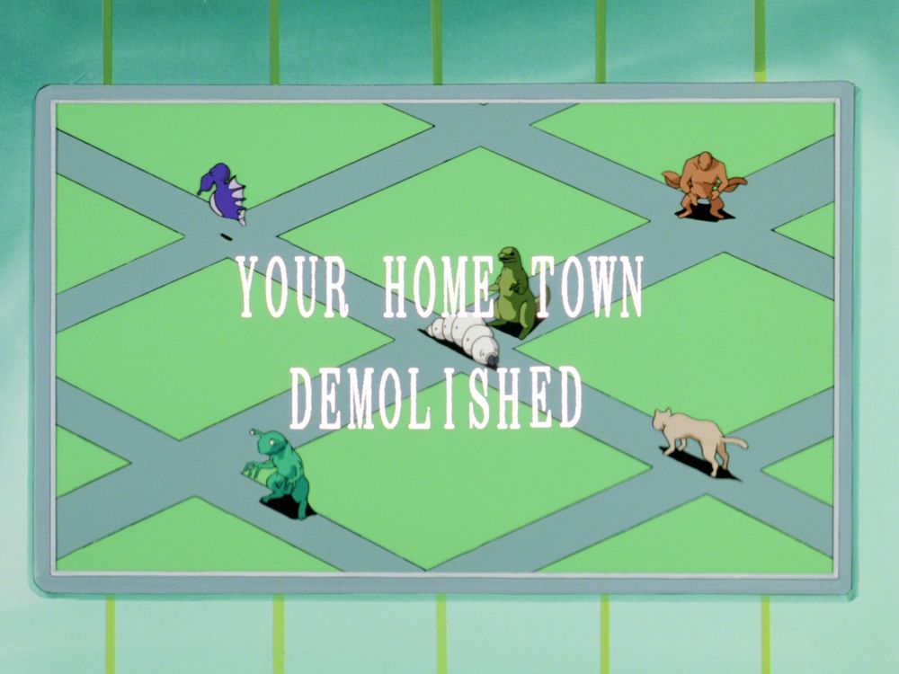 Picture with various giant monsters and a domestic cat on top of several empty, flat blocks of city. It bears the text:
YOUR HOME TOWN
DEMOLISHED