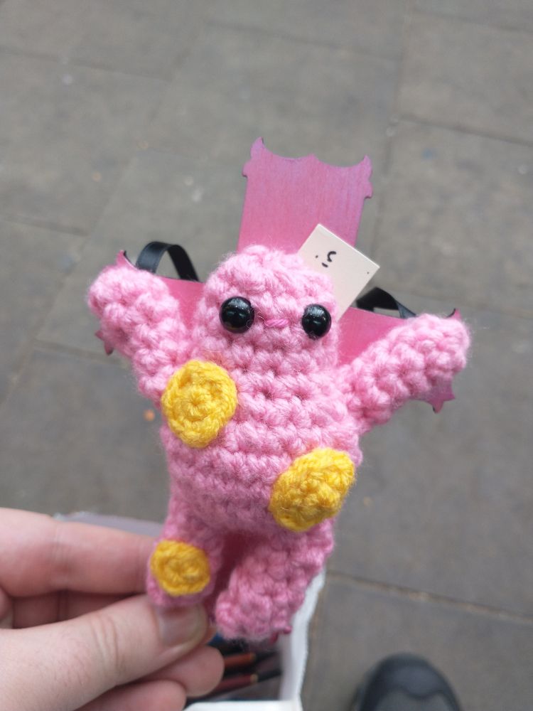 A crocheted Mr Blobby on a pink wooden cross, for our sins 