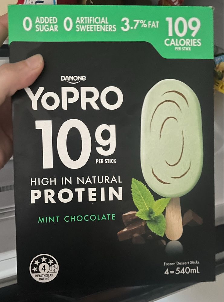 Photo of a box of individual ice creams held with one hand, in front of an open freezer. Text on the box reads “0 added sugar 0 artificial sweeteners 3.7% fat 109 calories”
“Danone YoPRO 10g per stick high in natural protein. Mint chocolate”