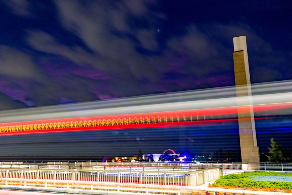 A photo of the National museum in Canberra with the lights from a bus in the foreground. Taken at lake burley griffin at commonwealth avenue bridge. 