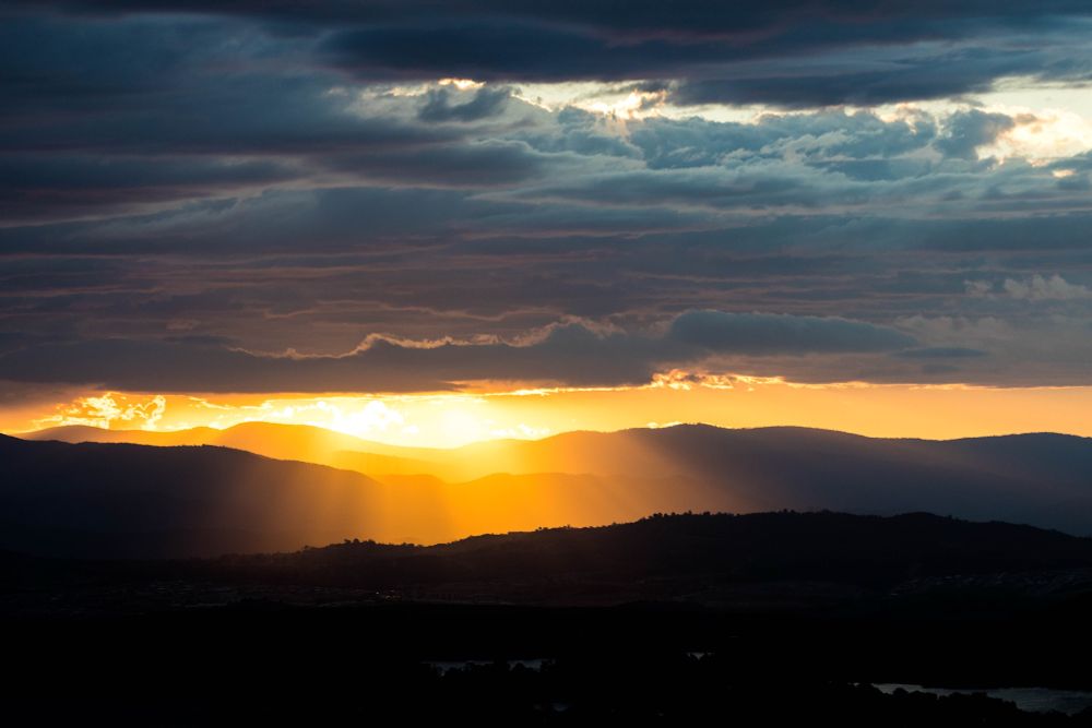 The sun coming through the clouds in a landscape photo of a mountain range