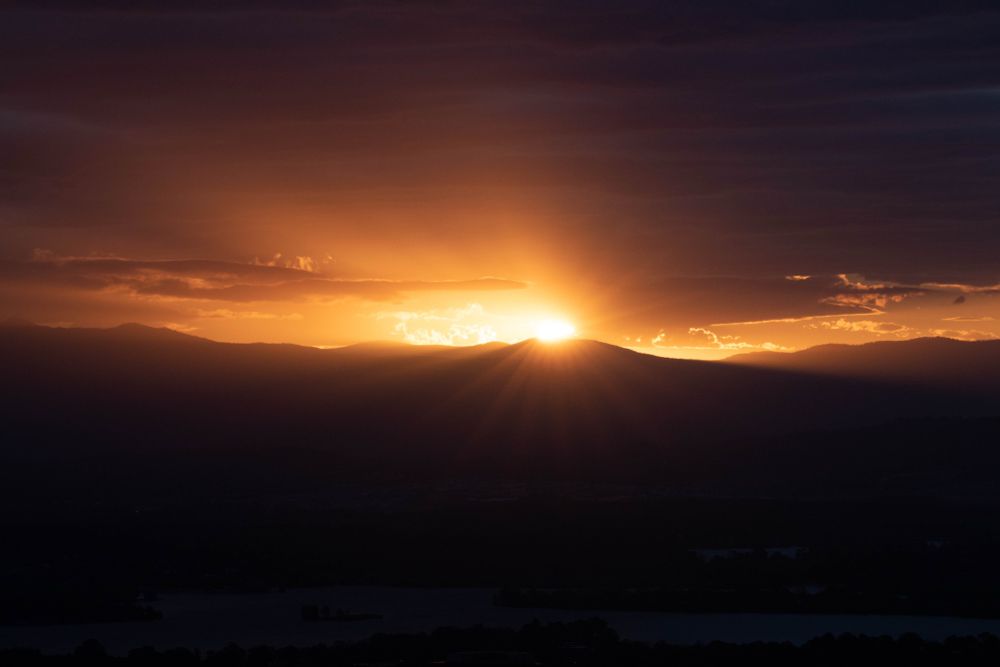A mountain at sunset. The sun is just peeking over the hill with sun rays visible