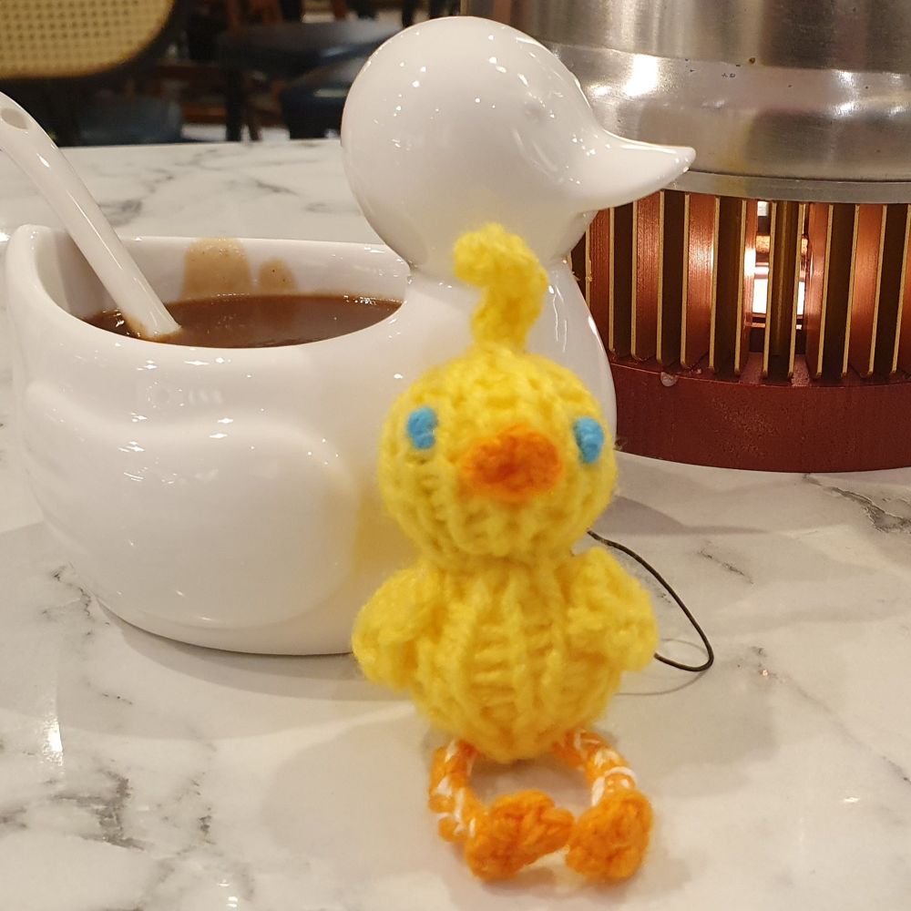ahiru sitting in front of a duck-shaped bowl for plum sauce, next to a teapot warmer with the tealight flame peeking through the slats of the teapot stand