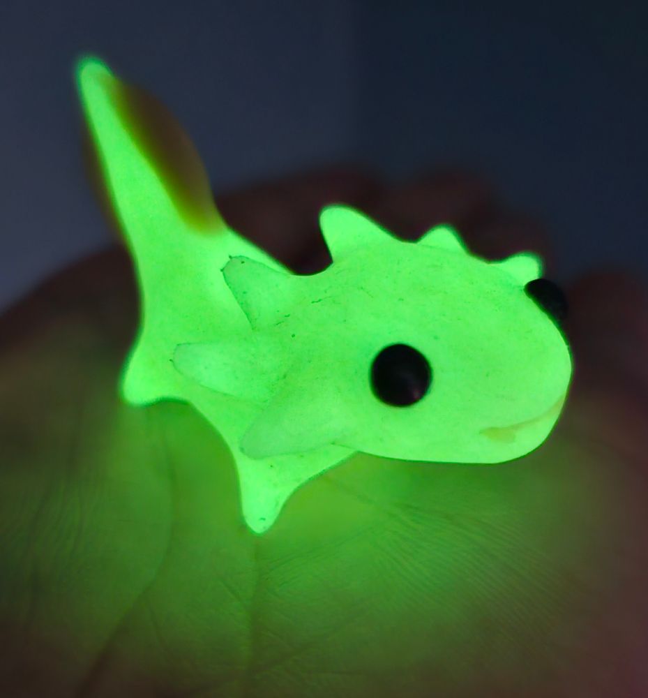 A small clay sculpture of an axolotl, glowing bright green sitting on my hand in the dark.
