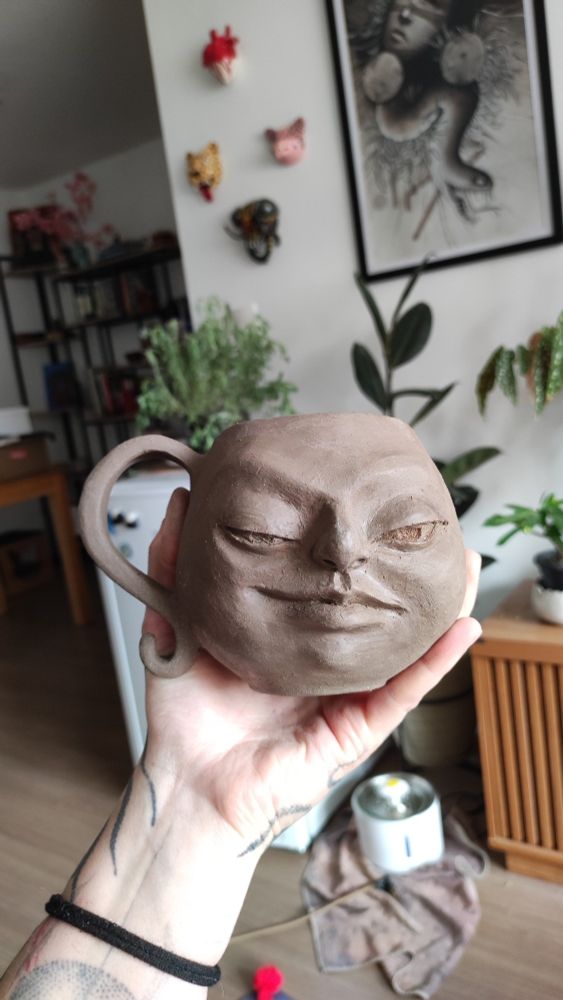 Caneca de argila modelada a mão com um rosto esculpido com expressão desafiadora