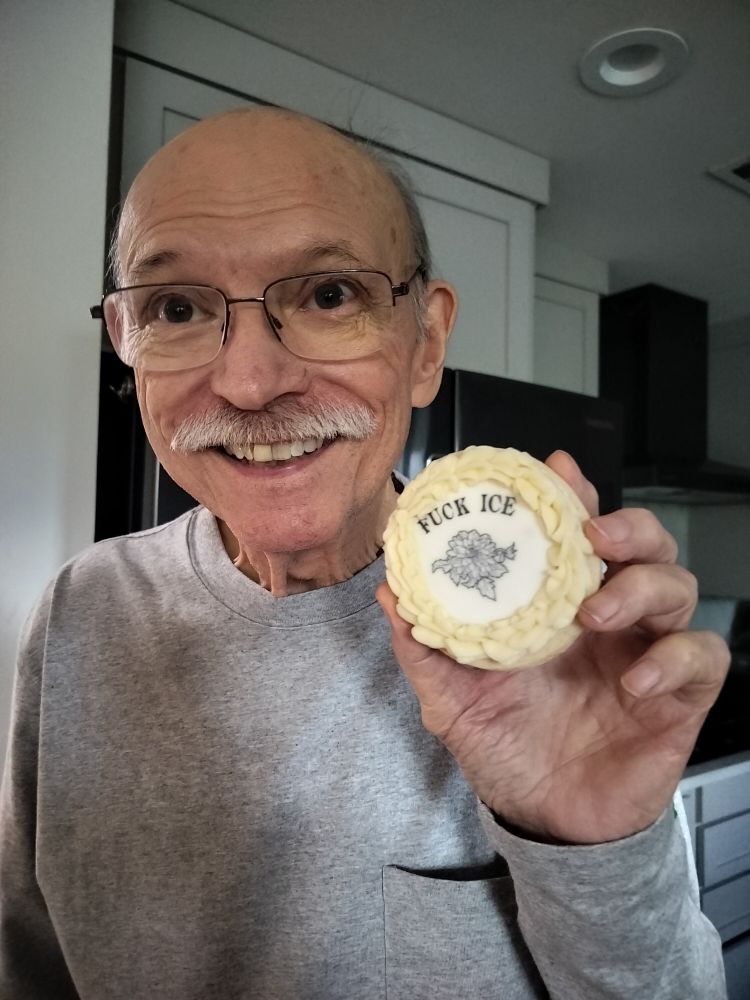 Smiling older man with moustache holding a cookie that says "fuck ice"