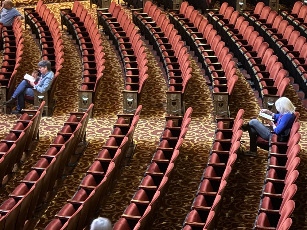An empty theater with 2 people seated 5 rows apart, each reading a book