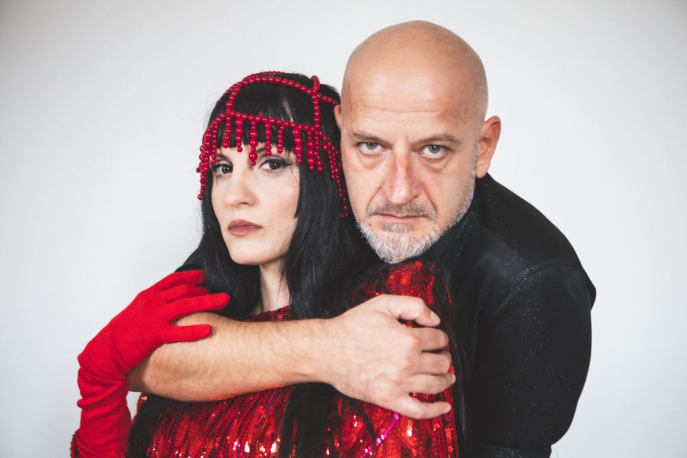 A white man in black shirt holds a woman with black hair wearing red