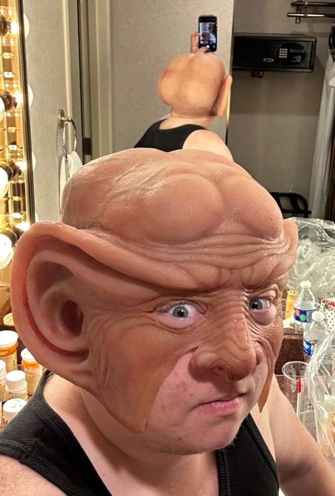 A selfie of me in the hotel bathroom mirror, wearing the Ferengi prosthetic without glue or makeup. I am facing the camera, but the back of the prosthetic head is visible in the mirror behind me. 