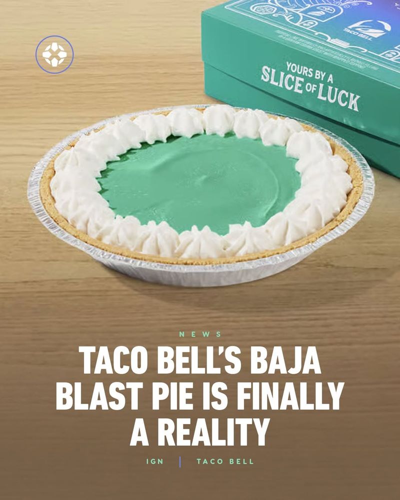A promotional image showing Taco Bell’s new Baja Blast Pie. The pie has a bright teal-blue filling that matches the color of the Baja Blast drink, surrounded by whipped cream along the edge, and sits in a graham cracker crust inside a foil pie tin. Behind it is a teal box with the text “Yours by a Slice of Luck.” The headline reads: “Taco Bell’s Baja Blast Pie Is Finally a Reality — IGN | Taco Bell.”
