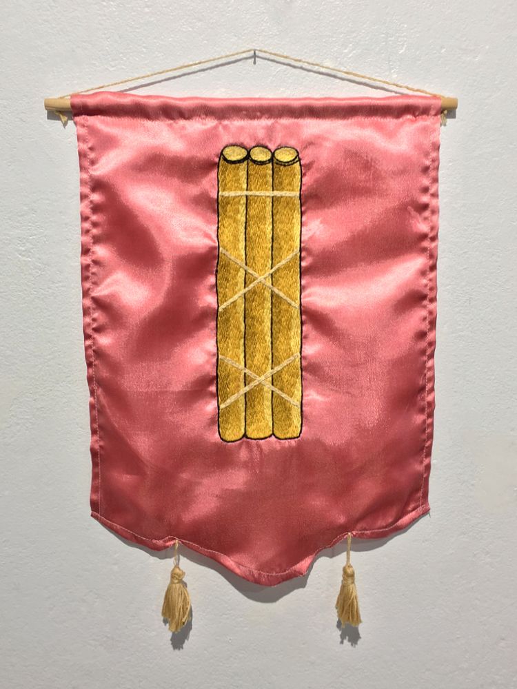 An embroidery of a bundle of sticks on a pink satin fabric