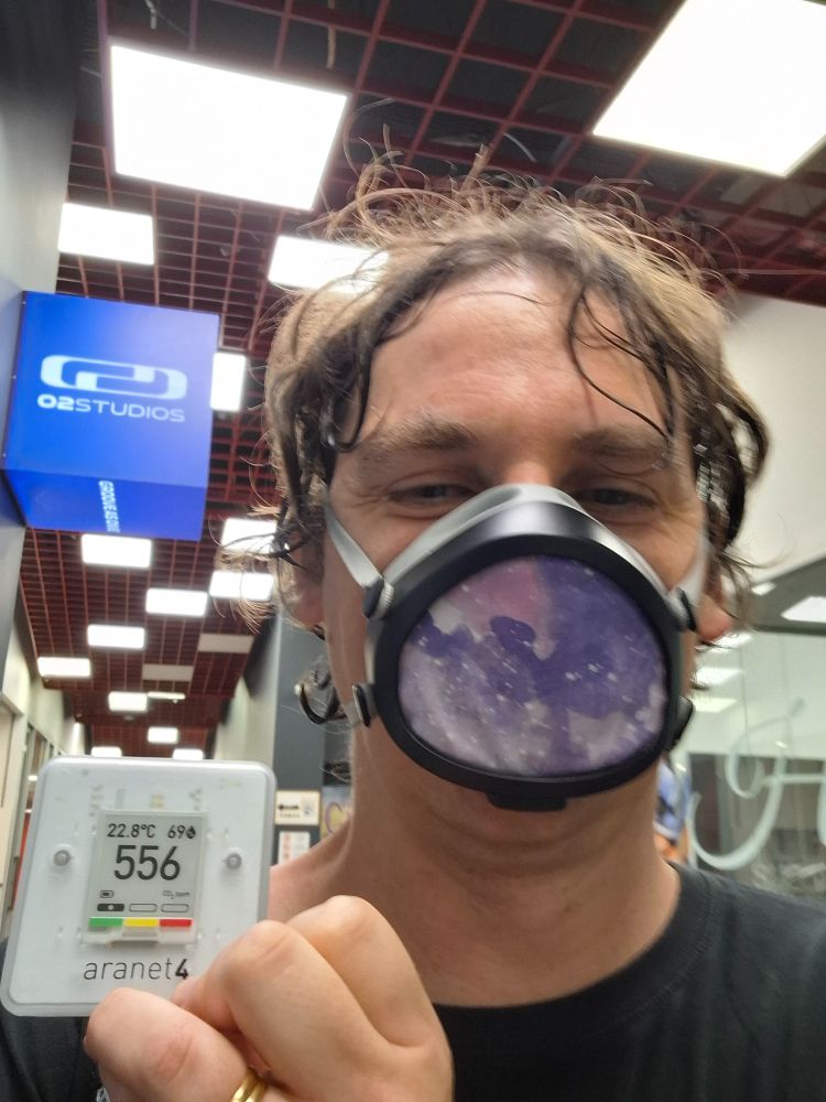 Man holding a CO2 monitor that reads 556ppm and wearing a Flo mask next to a sign for O2 Dance Studios