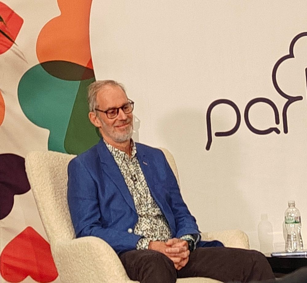 Paul Sinton Hewitt, blue jacket, patterned shirt, wry smile.