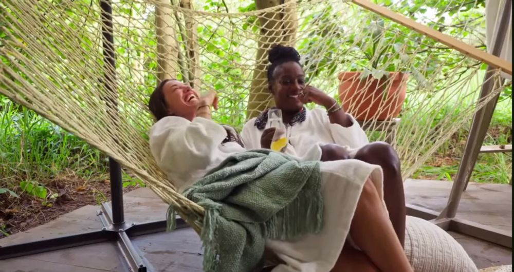 two women parvati shallow and Cirie Fields from survivor australia vs the world, sitting in a hammock in white robes laughing together 