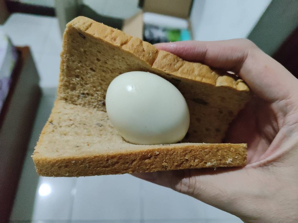 hand holding a folded slice of bread, hard boiled egg in the middle
