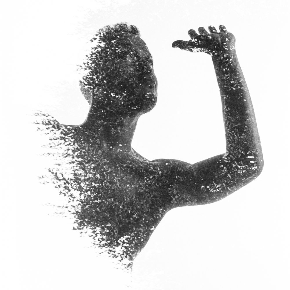 Upper body of a man, pushing his left arm up. His torso fades into foliage from the double exposure. Black and white. 