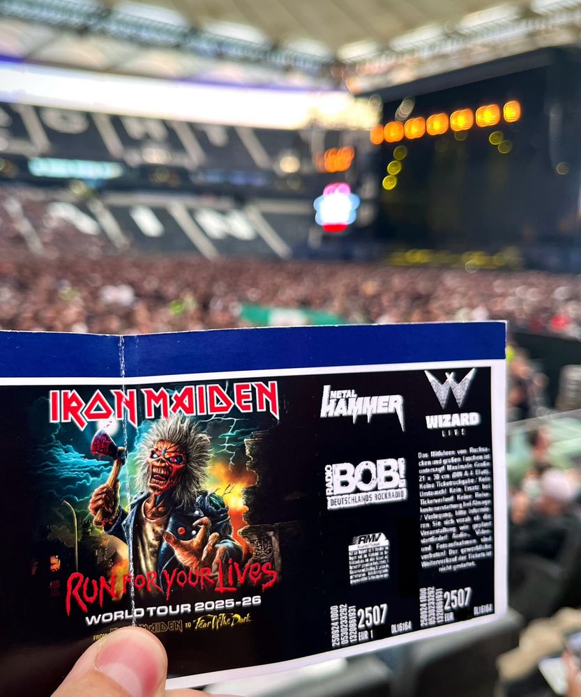 Hand holding a paper ticket at an Iron Maiden concert. 