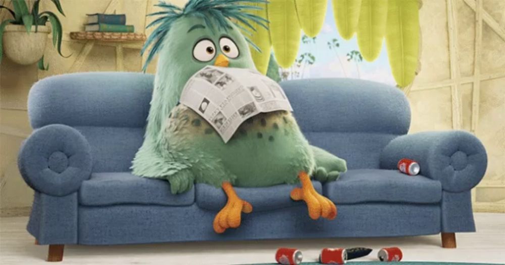 a green stuffed animal is sitting on a blue couch reading a newspaper