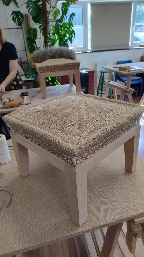 The first stuffing of an upholstered foot stool, with rows of stitching around the edges to hold the stuffing in place and create the structure and shape