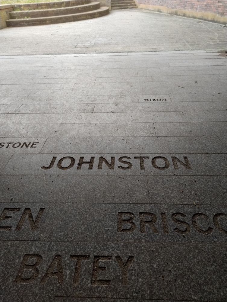 A close up of the pavement in a gloomy underpass, focused on the name Johnston carved into the stone slabs.