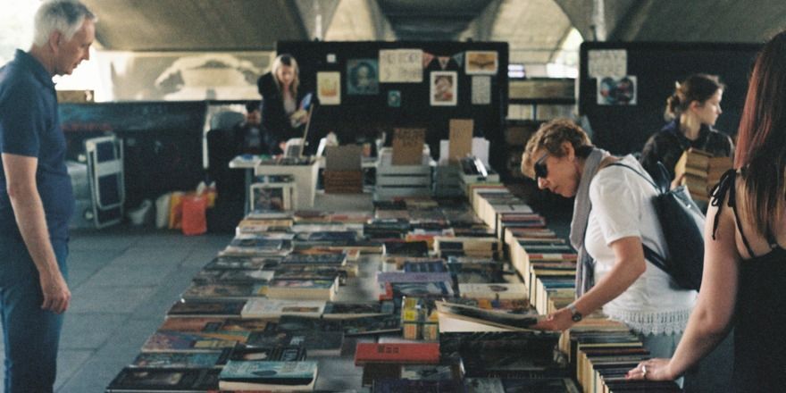 Several people of mixed ages and genders examine books stacked on a long table.