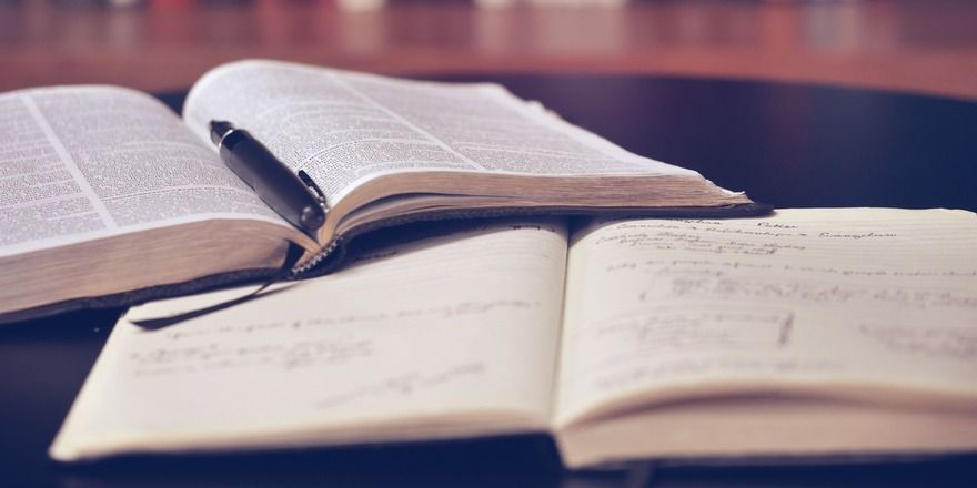 A notebook that's been written in heavily lies open next to a reference book that's also open with a pen resting on top of it.