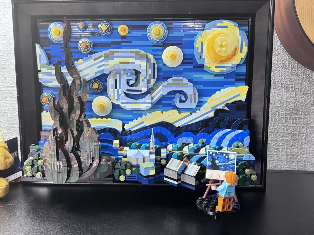 Completed Lego representation of Van Gogh's "Starry night" painting, an impressionist painting of a small town at night, with tall cypress tree, and swirling sky in shades of blue with large yellow stars, and yellow full moon.