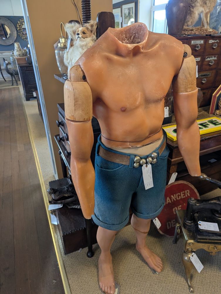 A wax wooden headless shirtless statue wearing shorts.