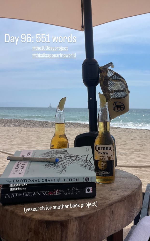 Two coronas with lime, two books, one pen on a table under an umbrella on a beach in Puerto Vallarta. 