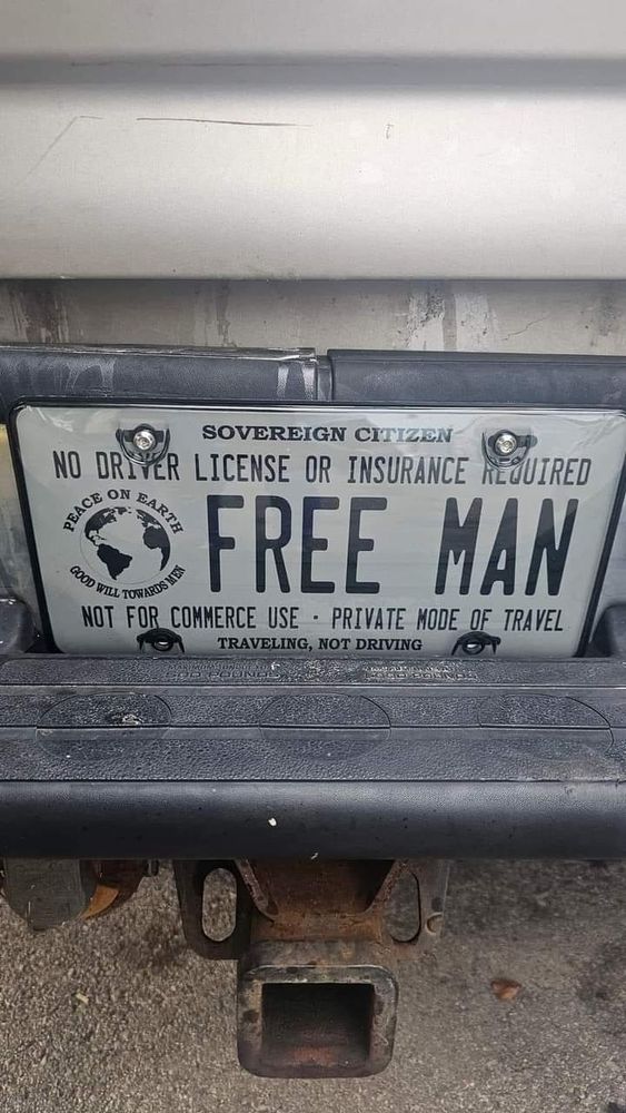 A pic of a fake license plate full of Sovereign Citizen nonsense. "No driver license or insurance required. FREE MAN. Not for commerce use. Private mode of travel. Traveling, not driving."