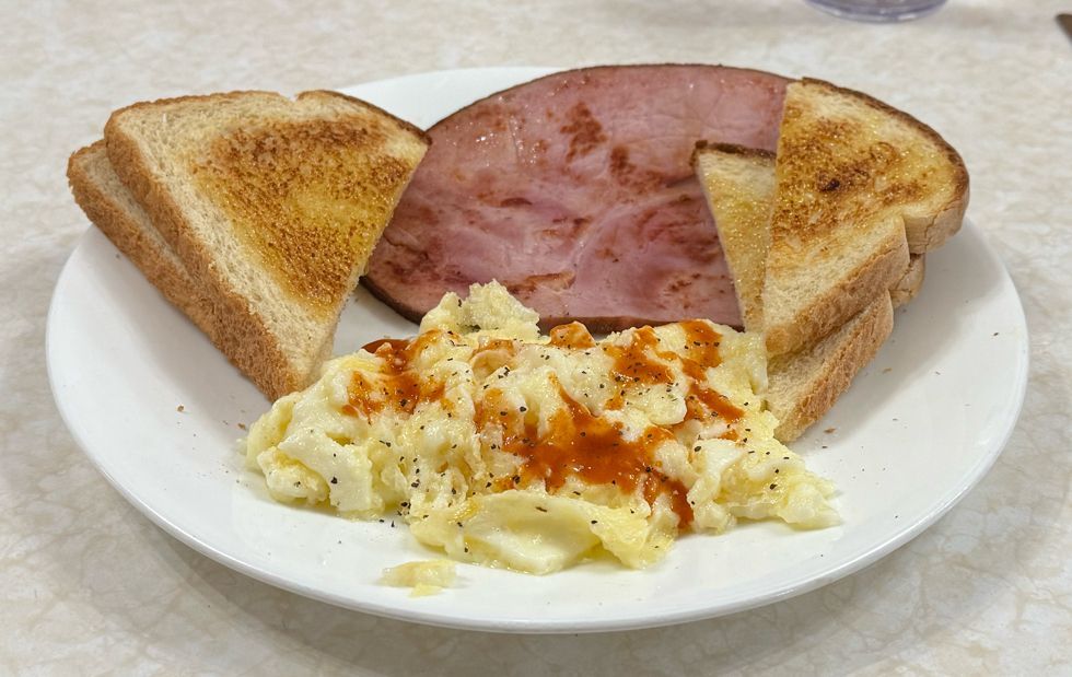 Breakfast at a diner. The plate has egg whites covered with hot sauce and pepper, grilled ham, and a couple of slices of buttered sourdough toast.
