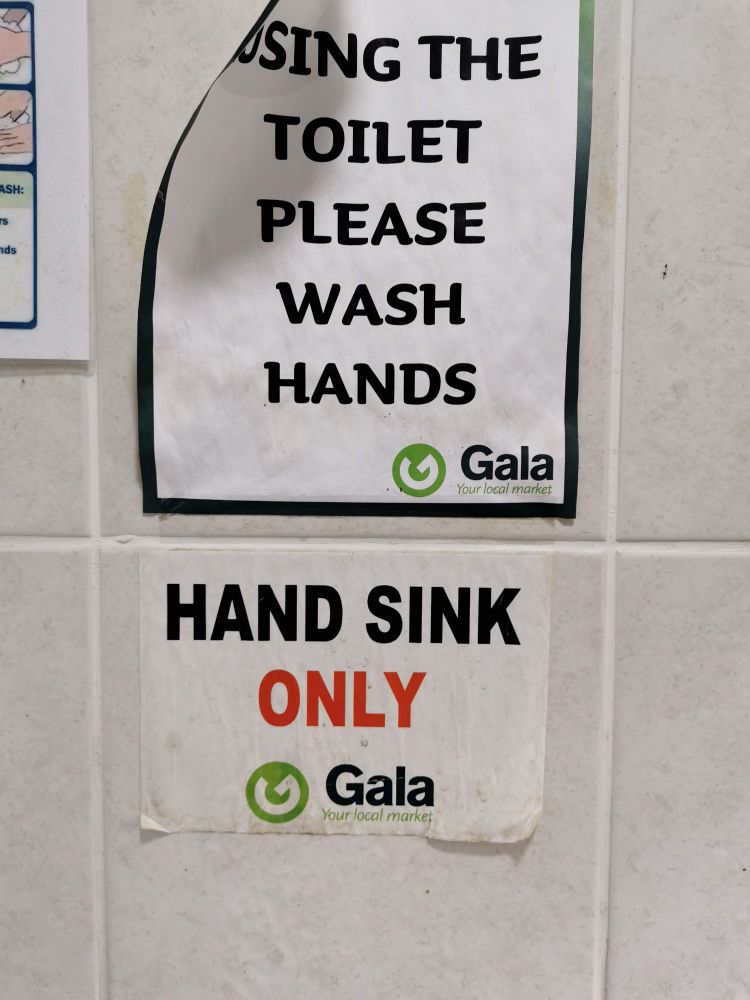 Signs from a wall of white tile in a public bathroom.
Top poster says in black test "Using the toilet  please wash hands"
Second poster says "Hand Sink (in black text) Only (in red text)" 