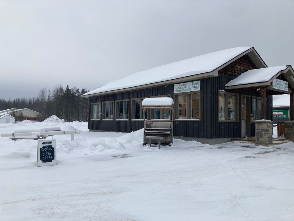 Single story black building with upright piano outdoors, signage and pipes in the snow.  Taken at NAISA North Media Arts Centre in South River, Canada.