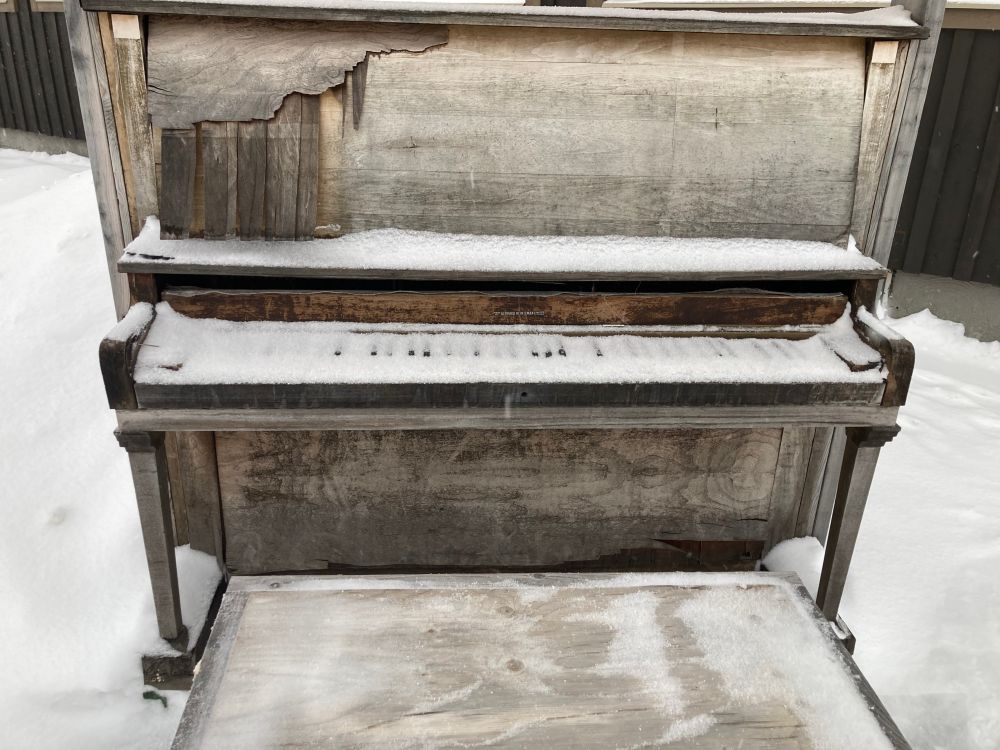 upright piano aged from weather with keys covered in snow.