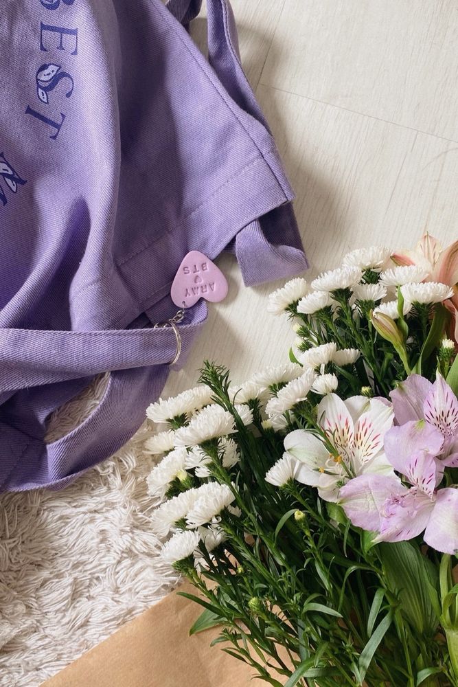 Ecobag roxa disposta no chão com um buquê de astromélias e áster