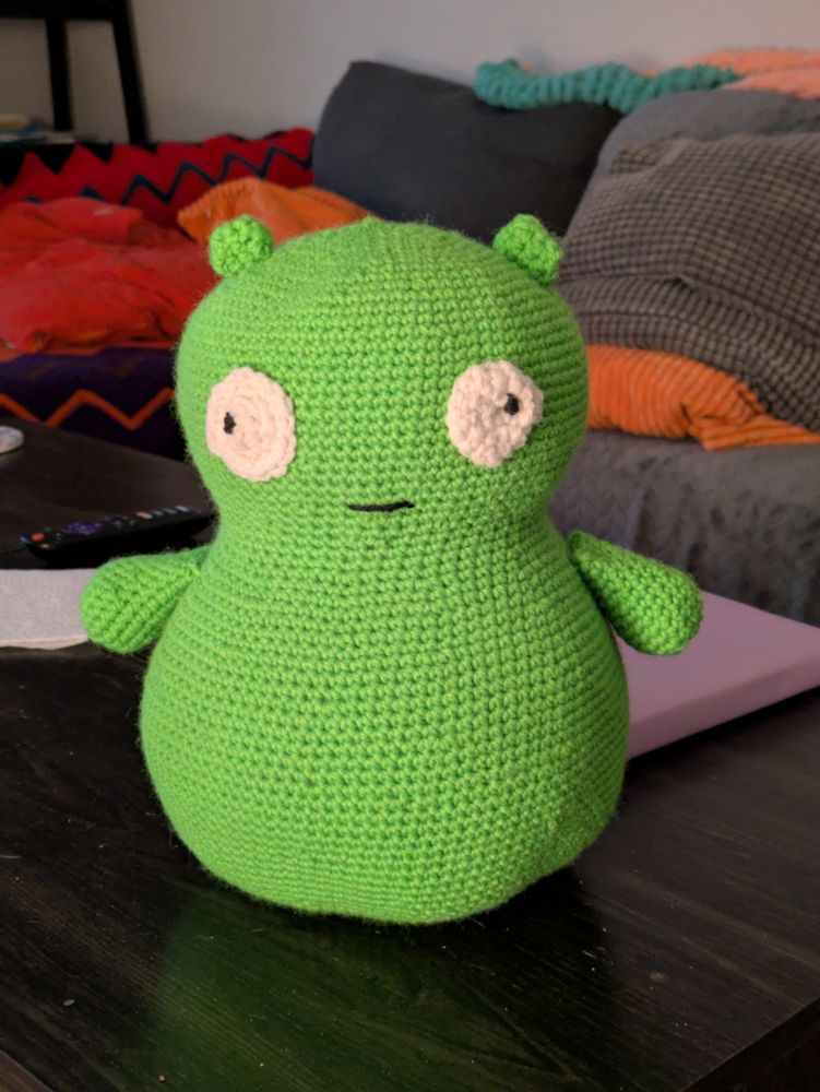 A crocheted Kopi Kuchi amurigurumi toy sits on a black table.