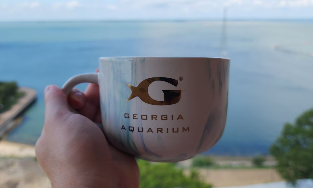 Holding up a cup of coffee next to the ocean
The cup says Georgia aquarium on it