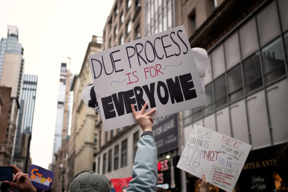 Photo of a hand holding a protest sign that reads "Due process is for everyone."