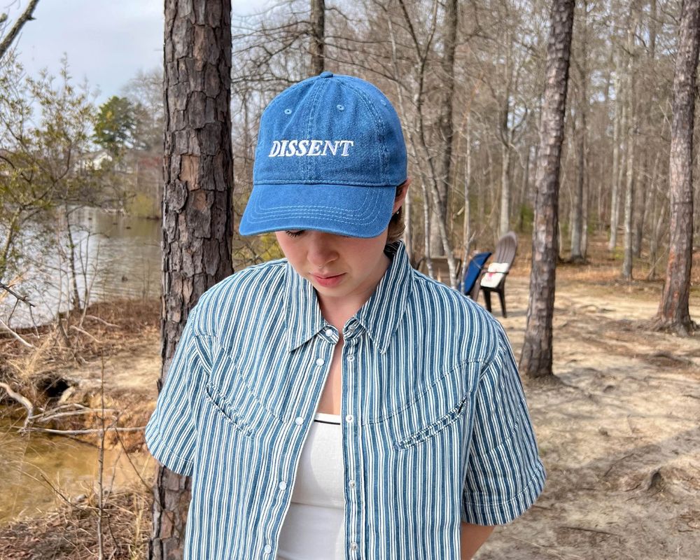 Image of a person looking down wearing a blue denim dissent hat.